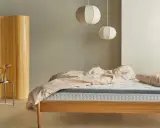 Una habitación nórdica con cama de madera, ropa de cama rosa y un biombo de bambú.