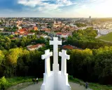 Wzgórze Trzech Krzyży w Wilnie z widokiem na miasto. Trzy białe krzyże górują nad zielonymi drzewami i zabytkową architekturą.