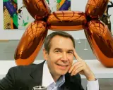 Jeff Koons posa junto a su icónica escultura perro globo naranja brillante en una galería de arte.