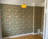 Ett rum med blommig tapet och en gul lampa. Undrar vad kostar det att måla om ett rum?