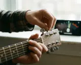 Main d'un musicien ajustant une guitare accordée, avec un accordeur sur un téléphone en arrière-plan.