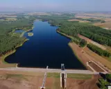 Widok z lotu ptaka na zalew Jagodno otoczony lasem i polami. Na pierwszym planie zapora z budowlami technicznymi.