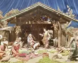 Krippenszene mit Maria, Josef und dem Jesuskind. Engel schweben über der Szene, die an Weihnachten im Mittelalter erinnert. Hirten und Musiker sind versammelt.