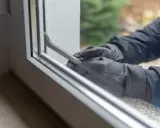 Manos enguantadas forzando una ventana de seguridad con una palanca.