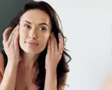 Mujer se toca la cara, examinando su piel. No se observa ninguna cara inflamada.