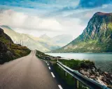 En slingrande väg leder mot dramatiska berg och en glittrande fjord. Drömmer om resor till Lofoten.