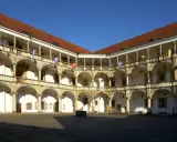 Dziedziniec renesansowego zamku z arkadowymi krużgankami, ozdobiony flagami.