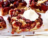 Saftiger Pflaumenkuchen mit Streuseln und einem Klecks Sahne. Ein Stück Kuchen liegt auf einem Messer, daneben eine Schale mit Sahne.