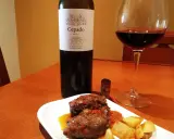 Un plato de carrilleras estofadas con patatas, acompañado de una copa de vino tinto Cepado Mencía, ideal para maridar.