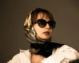 Donna con occhiali da sole e un elegante outfit con foulard annodato al collo, che incornicia il viso.