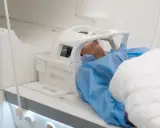 Pacjent w niebieskim fartuchu leży w aparacie MRI. Czas badania, czyli ile trwa rezonans głowy, zależy od wielu czynników.