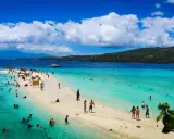 Plaża na Filipinach z turystami kąpiącymi się w turkusowej wodzie i spacerującymi po piaszczystym brzegu.