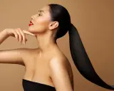 Frau mit glänzendem, schwarzem Pferdeschwanz und rotem Lippenstift, die ihren Hals berührt. Ihr **sleek look** unterstreicht ihre Eleganz.