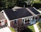 Ett hus med mörka solceller på taket, som fångar solens energi för ett grönare hem.