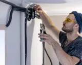 Elektryk w okularach ochronnych montuje przewody bezhalogenowe w puszce instalacyjnej, używając szczypiec.