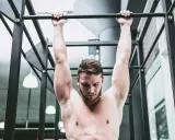 Uomo a torso nudo esegue trazioni alla sbarra, concentrato sul movimento per rafforzare la muscolatura.