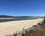 Gente disfrutando del sol y el agua en la playa de Arija, con montañas al fondo y un cielo azul despejado.