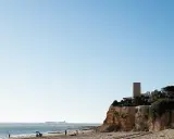 Sonniger Tag am **Playa La Barrosa**. Menschen genießen den Strand, während im Hintergrund eine Festung am Meer thront.