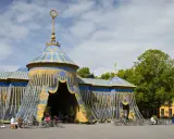 Blå och guldfärgad cirkustältliknande byggnad med uteservering i Haga parken.