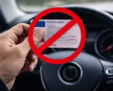 Zakaz prowadzenia pojazdów mechanicznych na 3 lata. Co dalej? Ręka trzyma prawo jazdy pod czerwonym znakiem zakazu, na tle kierownicy samochodu.