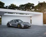 Silberner Porsche Turbo S, bereit für den 0-100 Sprint, parkt vor moderner Architektur im Sonnenuntergang.