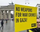 Gelbe Tafel mit Aufschrift "NO WEAPONS FOR WAR CRIMES IN GAZA!" vor dem Brandenburger Tor. Amnesty International setzt sich für Menschenrechte ein.