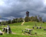 Drewniana wieża widokowa na Lubaniu. Trasa prowadzi przez zielone wzgórza pod burzowym niebem.