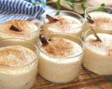 Seis copas de cremoso arroz con leche, espolvoreado con canela y decorado con una rama de canela.