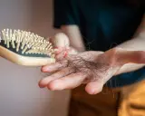 Main d'une personne tenant une brosse à cheveux avec des cheveux tombés, un effet secondaire possible du covid et perte de cheveux.