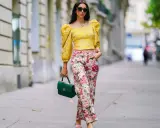 A woman shows that a woman can wear pants for cocktail attire, sporting a yellow puff-sleeve top and floral pants.