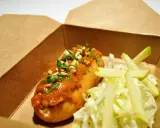 Un delicioso hot dog con salsa de cacahuete y cilantro, acompañado de ensalada de col y manzana, listo para tu delivery.