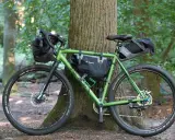 Grünes Gravelbike mit Taschen für Bike Packing, bereit für Abenteuer im Wald.