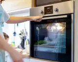 Une main ajuste la porte d'un four encastrable. La lumière intérieure est allumée, prêt pour la cuisson.