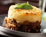 Un délicieux parmentier de canard, gratiné et garni d'une feuille de sauge, servi sur une assiette élégante.
