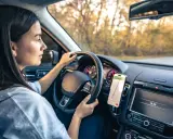 Kobieta prowadzi auto, a telefon z nawigacją zamontowany jest na desce rozdzielczej. Idealne miejsce, gdzie zamontować uchwyt na telefon w samochodzie.