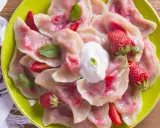 Pyszne pierogi z truskawkami, udekorowane miętą i śmietaną, na zielonym talerzu.