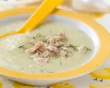 Un cremoso puré de verduras con pollo desmenuzado y eneldo, servido en un plato amarillo con una cuchara.