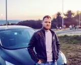 Mężczyzna w skórzanej kurtce opiera się o swój nowy samochód. To jego oc mubi, gotowy na przygodę.