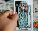 Dłoń trzyma kartę z tarot z 5 kart, przedstawiającą Wielką Kapłankę. W tle widać inne karty.
