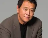 Robert Kiyosaki, autor "Bogatych ojców", w brązowej marynarce i czarnej koszulce, patrzy w obiektyw.