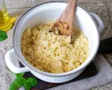 Frisch zubereiteter Couscous als Beilage in einem Topf, daneben ein Glas Öl und Minzblätter.