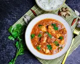 Ein Teller mit Hähnchen-Curry in cremiger **masala sauce**, garniert mit Koriander. Daneben Reis, Ingwer, Knoblauch und Chilis.