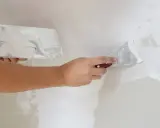 Persona aplicando masilla en una pared con dos espátulas. Aprende cómo masillar una pared para un acabado perfecto.