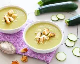 Deux bols de velouté de courgettes crémeux, garnis de croûtons dorés, avec des courgettes fraîches et des rondelles en arrière-plan.