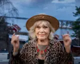 Christina Schollin, med sin karaktäristiska hatt och leopardmönstrade jacka, ser ut att berätta en historia från sina filmer och tv-program.