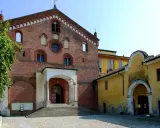 Morimondo cosa vedere: imponente facciata in mattoni rossi di un'antica abbazia, con scalinata e portico. Accanto, un edificio giallo con un arco.