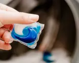 Mano sostiene una cápsula de detergente azul y blanca lista para usar en la lavadora.