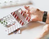 Dłoń starszej osoby trzyma opakowanie tabletek, obok leżą inne blistry. Może to być kwas foliowy B9.
