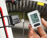 Rowerzysta sprawdza licznik pokazujący dystans 21.87 km. Obok widoczny czujnik na kole, który mierzy obwód koła rowerowego.