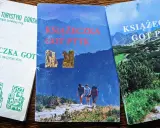 Trzy książeczki GOT PTTK z odznakami. Jedna biała z zielonymi symbolami, dwie z górskimi krajobrazami.
